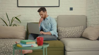 Bilgisayarda yazı yazan mutlu adam elini sallayan kameraya bak. Ev bilgisayarının modern oturma odasındaki koltukta oturan bir şeyi göstermek istiyor. Yavaş çekimde kapat.