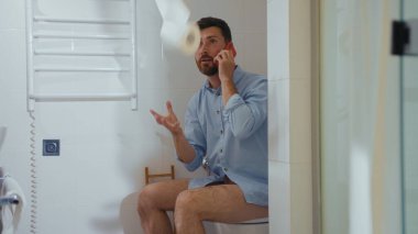 Komik mutlu iş adamı tuvalette oturup gülümseyen cep telefonu akıllı telefon internet ev tuvaletini kullanıyor.