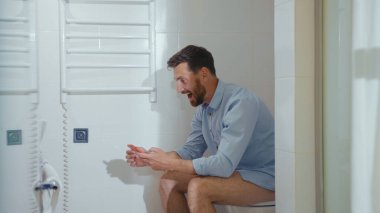 Mutlu iş adamı tuvalette oturup gülümseyen cep telefonu akıllı telefon internet ev tuvaleti yavaş çekim banyoyu kapatıyor.