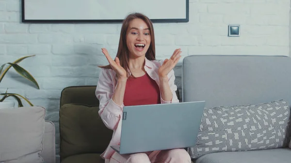 Cheerful young woman worker learns great news on laptop clapping hands to celebrate business success job achievement working from home.