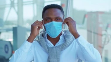 Afrika kökenli Amerikalı genç adam Koruyucu Yüz Maskesi 'ni kaldırıyor ve kameraya ciddi bir şekilde bakıyor. COVID-19 koronavirüs enfeksiyonu. Salgın hastalık salgını. Yavaş çekim