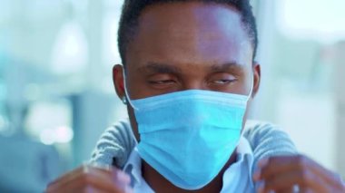 Gülümseyen Afrikalı Amerikalı genç adam Koruyucu Yüz Maskesi 'ni kaldırıyor ve kameraya mutlu bir şekilde bakıyor. COVID-19 koronavirüs enfeksiyonu. Salgın hastalık salgını. Yavaş çekim