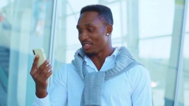 Genç Afro-Amerikalı adam havaalanının yakınındaki telefon kulübesinde görüntülü konuşma için akıllı telefon kullanıyor. Kendine güvenen lider portresi. Açık havada. Yavaş çekim