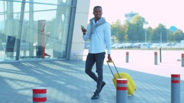 Portre, genç Afro-Amerikalı iş adamının sarı bavulla havaalanı yakınlarında mutlu bir şekilde gülümsediğini gösteriyor. Güven yarışı başarısı çekici. Kapatın. Yavaş çekim