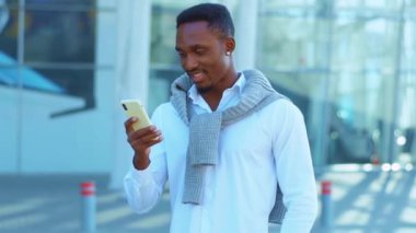 Mutlu Afrikalı Amerikalı adam havaalanının yakınındaki akıllı telefon standında gülümseyen bir mesaj yazıyor. Kendine güvenen genç bir lider portresi. Açık havada. Yavaş çekim