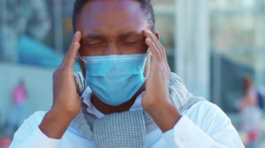 Yüzüne koruyucu maske takan Afro-Amerikan adam havaalanının yakınlarında baş ağrısı çekiyor. COVID-19 koronavirüs enfeksiyonu. Salgın hastalık. Turist salgını. Yavaş çekim