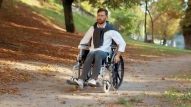 Genç adam güneş ışığında parktaki tekerlekli sandalyelerde sakat. Felç engelli sakat. Çok ciddiyim. Sonbahar geldi. Yavaş çekim