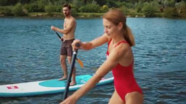 Çekici erkek ve kadın yemek masasında durur ve yüzme sporu sörfçüleri için bir kürekle gölde yüzer arkadaşlar yavaş çekim yaklaşır.