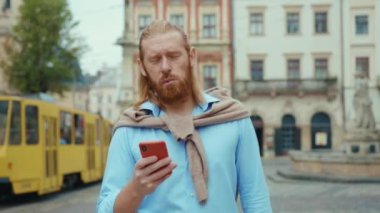 Yakışıklı kızıl saçlı, stil sahibi hippi adam güzel şehir merkezinde sokakta cep telefonu iletişim uygulaması kullanıyor. İş adamları. Çekici kızıl..