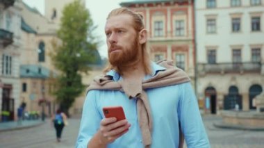 Ciddi sakallı, uzun kızıl saçlı, akıllı telefon kullanan sosyal medyada haberleşen mesajlar yazan iş adamı şehir merkezinde yürüyor..