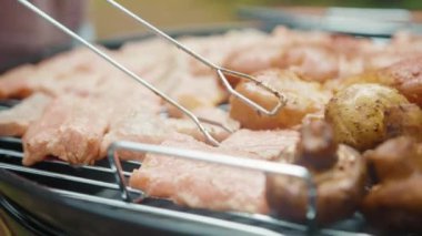 Kömür ezicisinde ızgara somon ısırığı ve mantar. Biftek parçalarını yanan kömürün üzerinde salamura ile çeviren adamın yakın çekimi. Piknik. Barbekü.