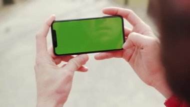 Los Angeles, Kaliforniya 15 03: 2019 Yavaş çekim adamı yeşil ekran yatay arka plan parkı dijital ekran internet akıllı telefon ile duruyor ve telefona dokunuyor.