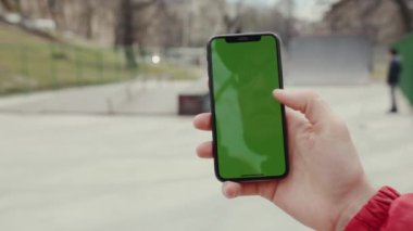 Los Angeles, California 15 03 2019 EDITORIAL: Yeşil ekran dikey arka planlı telefona dokunan genç adam aktif park şehri dijital ekran akıllı telefon