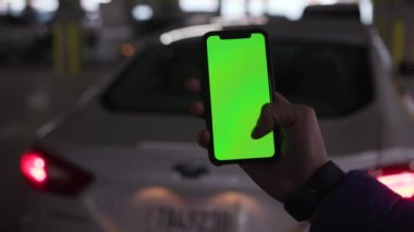 Los Angeles, Kaliforniya 15 03 03 2019 EDITORIAL: Elinde yeşil ekranlı cep telefonu tutan adam mobil uygulama ile mesaj atıyor. Beyaz arabanın arka planında akıllı telefon kullanan bir erkek. Bulanık. Kapalı