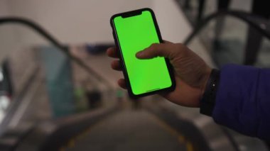 Los Angeles, California 15 03 2019 EDITORIAL: metrodaki yürüyen merdivenin arka planında yeşil ekranlı akıllı telefon kullanan mavi ceketli bir erkek. Parmak, teknoloji, dokunma. Kapalı.