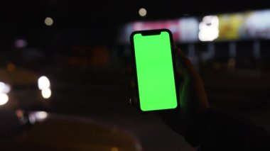 Los Angeles, Kaliforniya 15 03 03 2019 EDITORIAL: Arkaplanda genç bir kişinin elinde yeşil ekranda reklam panoları ve arabanın bulanık görüntüsü. Gece vakti. Açık havada. Gadget, cep telefonu.