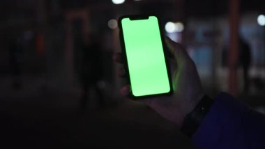 Los Angeles, California 15 03 2019 EDITORIAL: metro çıkışının bulanık arka planında boş yeşil ekranlı cep telefonu tutan adam. Dokun. Bokeh ışıkları, işaret eden parmak. Açık havada..