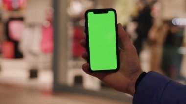 Los Angeles, Kaliforniya 15 03: 2019 İnsan eli akıllı telefonu yeşil ekran parmağıyla tutuyor kromakey dokunmatik dokunmatik kaydırma ekranı, alışveriş merkezindeki bulanık arka plana dokunuyor.