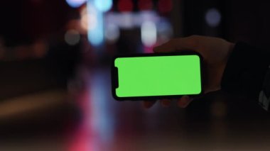 Los Angeles, California 15 03 03 2019 EDITORIAL: Gece lambası arka planında yatay olarak modern akıllı telefon tutan adam. Yeşil ekran. İnternette sörf yapmak, sosyal ağlara bakmak,