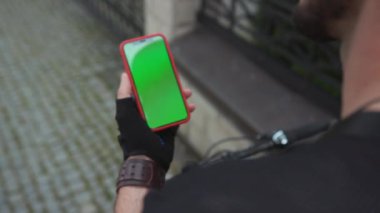 NEW YORK - 15 Haziran 2019: Bisiklet süren genç bir sporcu sokakta yürüyor ve açık havada akıllı telefondan yeşil ekran krom anahtar kullanıyor..