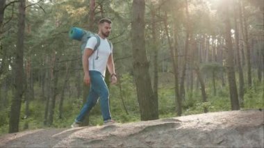 Ormanda tek başına gülen yakışıklı genç adam yürüyüşçüsü yalnız başına orman yürüyüşü genç tatil çekici sonbahar yürüyüşçüsü ağır çekimde seyahat ediyor.