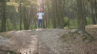 Gülümseyen yakışıklı genç adam ormanda duruyor. Güneş ışığına mutlu bir şekilde bakıyor. Yalnız başına orman yürüyüşü yapıyor.