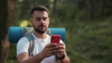 Ormanda sakallı ve sırt çantalı ağır çekimli bir adam bağlantı sinyali aramak için telefonu kullanıyor. GPS başvurusu, turizm turizmi yürüyüşü, kayıp güneş iletişimi telefonu, yakın çekim.