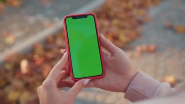 NEW YORK - 5 Nisan 2019: Güneşli bir günde elinde yeşil ekranlı dikey telefon tutan kadın internet teknolojisi akıllı telefon kroma anahtar mesajı ile sörf sayfalarını kaydırıyor