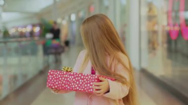 Noel hediyesi kutularıyla alışveriş merkezinde yürüyen sevimli bir kız. Çocuk, aile, güzel çocuklar, neşeli, mutlu bir tatil çocuğu. Yavaş çekimde gülümsüyor.