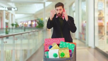 Noel hediyesi kutularıyla öfkeli sakallı bir adam alışveriş merkezinde telefonla konuşuyor. Noel ağacı alışverişi yapıyor. Yüzü mobil hücreyi yavaş çekimde kapatıyor.