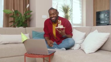 Afrikalı Amerikalı adam doğum gününü karantina sırasında kutluyor. Web kamerasından mumlar üflüyor ve aile üyeleriyle çevrimiçi iletişim kuruyor. Evde doğum günü. Bir kişi. Kişisel izolasyon.