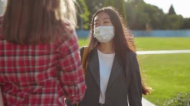 İki kız dışarıda yüz maskeleriyle iletişim kuruyor. İki çok ırklı kız öğrenci kampüsün yakınında kursları tartışıyorlar. Eğitim. Kız arkadaşlar..