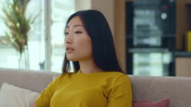 Asyalı genç ve çekici bir kadının gülümseyen portresi evdeki kanepede oturan kameraya bakıyor. Mutlu ol, başarılı ol. Seksi kızmış. Kapatın. Yavaş çekim