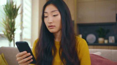 Şirin Asyalı genç bayan evdeki koltukta otururken telefon kullanıyor. Sosyal medya mesajları uzak iletişimin tadını çıkarıyor. Sosyal medya. Kapatın. Yavaş çekim
