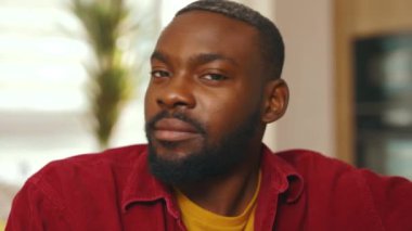 Genç, yakışıklı, Afro-Amerikan bir adam kameraya bakıp gülümsüyor ve evdeki kanepede oturuyor. Rahat ol. Çekici bir adam. Kapatın. Yavaş çekim