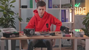 Evdeki ekipmanlardan İHA üzerinde çalışan ciddi bir beyaz adamın görüntüsü. Konsantre öğrenci masada oturuyor ve cihazın bir parçasını inceliyor. Gerekli parçalar. Modern teknoloji konsepti. Drone tipi.