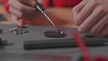 Erkek ellerinin lehim demirini tutarken ve lehim kablolarını bordaya yerleştirirken, insansız hava aracı parçalarken. Kafkasyalı genç bir adamın modern kuadkopteri iş başında inşa edişinin görüntüleri. İçeride. Araştırma ekipmanları, yüksek kaliteli işler. Gündüz.