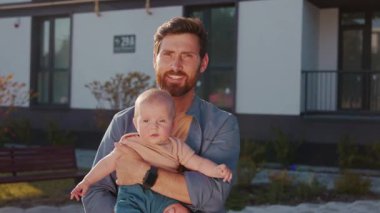 Mutlu bir babanın portresi yeni doğmuş bir bebeği güneş ışığında sokakta tutuyor. Gülümseyen adam. - Baba? Ebeveynlik. Babalık. Yavaş çekim