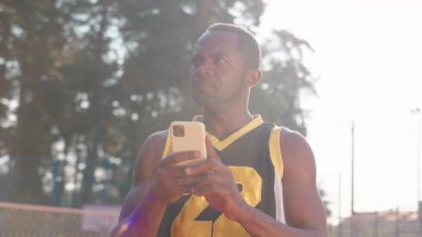 Şehir sahasında cep telefonu kullanan ciddi bir Afrikalı Amerikalının portresi. Çekici, düşünceli sakallı basketbolcunun bakışları. Açık havada. Gündüz, iletişim, aygıt