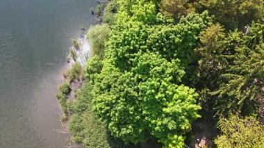 Sakin orman gölünün üzerindeki güneşin doğuşunu gösteren muhteşem bir hava aracı. Bulutlar suya yansıyor. Kapat.