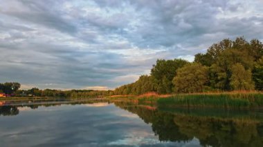 Sakin orman gölünün üzerinde güneşin doğuşunu gösteren güzel bir hava aracı. Bulutlar suya yansıyor. Kapat..