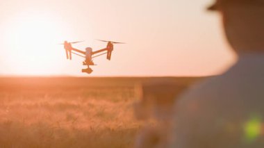 Gün batımında buğday tarlasında dijital kamerayla uçan dron çekimi. Şehir dışında Quadcopter kullanan tanımlanamayan bir adamın yakın çekim görüntüleri. Tarım kavramı