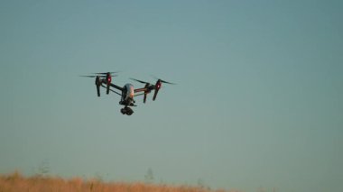 Mavi gökyüzünün arka planında beyaz İHA 'yı vurmak. Sahanın üzerinde dijital kamerayla uçan kuadkopter görüntüsü. Modern teknolojilerin tarımdaki kavramsal görüntüleri. Açık havada, yaz zamanı.