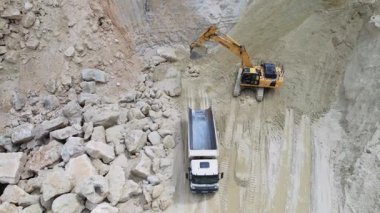 İnşaat alanında çöp kamyonunu kumla dolduran sarı sürüngen kazıcısının görüntüsü. Taş ocağı ve madencilik ekipmanlarının insansız hava aracı görüntüsü