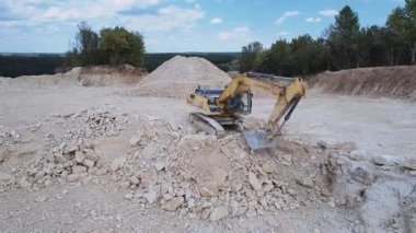 Sarı hareket eden böcek kazıcısının kovayı taşla doldurduğu görüntü. Madencilik endüstrisi, ulaşım. Taş ocağının insansız hava aracı görüntüsü. Ağır ekipman