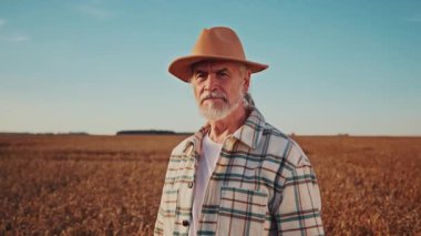 Yakından bakınca, şapkalı yakışıklı bir çiftçinin altın buğday tarlasında gülümseyerek mutlu olduğu görülüyor. Hasat. Tarım. Açık havada. Yavaş çekim