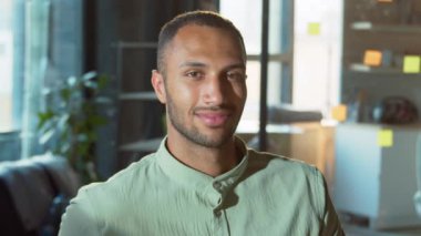 Kameraya bakan sıradan gömlekli mutlu Afrikalı adamın portresi. Ofiste dişlek gülümseyen bir adamın fotoğrafı. İşçi, iş, meslek. Güven, kariyer.