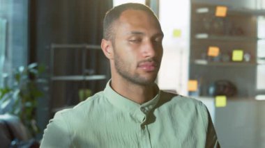 Başarılı, neşeli iş adamı kameraya bakıyor. Cam bir tahtanın arka planında, üzerinde yapışkan notlar olan sıradan giysili yakışıklı melez adamın portresi.