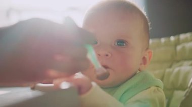 Meyve püresi içinde yüzü lekelenmiş, mutfakta kahvaltı yapan komik küçük çocuğu vurmak. Kaşığı tutan ve oğlunu besleyen kadın elleri. İçeride. Daire, ev.
