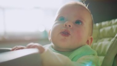 Kahvaltıda bebek maması yiyen yüzü lekeli komik küçük oğlan. Portatif yemek sandalyesinde oturan sevimli beyaz çocuk portresi. İçeride. Gün ışığı, gündüz. Mutfak, ev